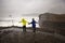 Children, standing at the edge of the ocean on heavy rain day near Dyrholaey, watching the huge waves, Iceland wintertime