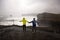 Children, standing at the edge of the ocean on heavy rain day near Dyrholaey, watching the huge waves, Iceland wintertime