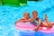 Children swiming on pink inflatable beach mattress at swimming pool.