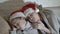Children, two little girls, in red hats of Santa Claus sleeping on the couch on each other covered with a blanket
