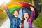 Children under umbrella enjoy to autumn rain outdoors.