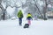 Children walking through a snowy neighborhood with a sled.
