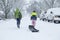 Children walking through a snowy neighborhood with a sled.