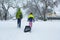 Children walking through a snowy neighborhood with a sled.