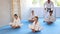 Children in white kimono sits in a butterfly pose and practices stretching in sport gym