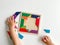 childs hand collects multicolored wooden mosaic on white background.