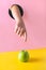 Childs hand through hole in pink paper reaches for green apple on yellow.Food concept