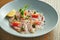 Chilled sea bass carpaccio with red onion, cherry tomatoes and hot chili peppers in a beige bowl on a wooden background. Close up