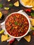 Chilli con Carne with tortilla chips and cheese in white bowl. Mexican food.