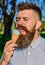 Chilling concept. Man with beard and mustache on calm face eats ice cream, nature background, defocused. Man with long