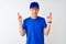 Chinese deliveryman wearing blue t-shirt and cap standing over isolated white background gesturing finger crossed smiling with