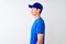 Chinese deliveryman wearing blue t-shirt and cap standing over isolated white background looking to side, relax profile pose with