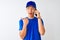Chinese deliveryman wearing cap talking on the smartphone over isolated white background pointing and showing with thumb up to the