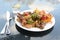 Chinese dish in a street restaurant, various meat and vegetables with fried rice on a white plate, cutlery and a glass with water