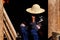 Chinese old women wearing traditional hat sits in wooden doors in morning light. She holding hat in hot weather. Yuanyang, Yunnan