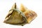 A Chinese sticky rice zongzi or bakcang, wrapped in bamboo leaves, and an unwrapped dumpling, on white background