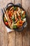 Chinese stir fry pork with broccoli, bok choy, carrots, peppers, cauliflower close-up in a pan. Vertical top view