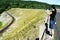 A Chinese woman taking pictures of a railroad track along an earthen dam