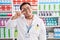 Chinese young man working at pharmacy drugstore doing peace symbol with fingers over face, smiling cheerful showing victory