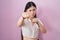 Chinese young woman standing over pink background punching fist to fight, aggressive and angry attack, threat and violence