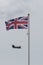 A chinook helicopter flying behind a union jack flag on a flag pole