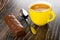 Chocolate bar with filling, yellow cup with coffee, spoon on wooden table