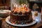 a chocolate birthday cake with lit candles on a table with plates of food and a glass of milk on the side of the table