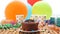 Chocolate birthday cake on rustic wooden table with background of colorful balloons, gifts, plastic cups with candies