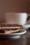 Chocolate biscuit snapped in half on a saucer in front of a white tea cup or coffee cup.