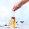 Chocolate brown ice cream in a regular yellow mug, on a blue background, the hand is poured crumbs. Unusual serve of dessert, copy