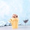 Chocolate brown ice cream in a regular yellow mug, on a blue background. Unusual serve of dessert, copy space