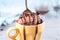 Chocolate brown ice cream in a regular yellow mug and spoon, on a blue background, with topping and crumbs. Unusual serve of