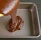 Chocolate Cake Batter Being Poured into Greased Cake Pan with Blurry Cake Mixture in Foreground