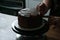 Chocolate cake being decorated by confectionery with chocolate plates. Main light from behind.