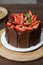 Chocolate cake covered with strawberries, basil leaves, blackberry jam and with chocolate plates around it. Wooden dish in the bac