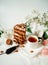 Chocolate cake decorated with various cookies and nuts on a glass plate and macaroons among white flowers of lilac and green