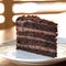 Chocolate cake. Piece of brown layered dessert with cream on white saucer. Sunny blurred background. Soft focus