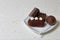 Chocolate cake pops and pieces of black chocolate on a white plate. Next to the potato cake. On the surface covered with white