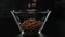 Chocolate cereal balls fall in a transparent square bowl on a black background. Close up.