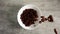 Chocolate cereal rings are falling into a white bowl standing on a wooden desk in slow motion