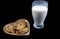 Chocolate chip cookies on a heart shaped plate with a glass of fresh milk on black background