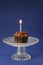 Chocolate cupcake with a burning candle on a glass bowl, blue background with copy space, birthday concept