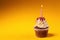 Chocolate cupcake with candle on orange background