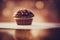 a chocolate cupcake with chocolate chips on top of it on a table with a blurry background of lights