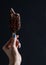 Chocolate dipped popsicle ice cream with chipped nuts held by woman\'s hand on black