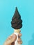 Chocolate-dipped soft-serve ice cream cone in hand against teal wall