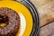 Chocolate donut on a yellow plate on a pink background