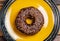Chocolate donut on a yellow plate on a pink background