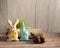 Chocolate eggs, funny handmade textile Easter bunnies and grass on a light wooden background.