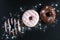 Chocolate and glazed donuts, pink, white, brown on black stone, top view